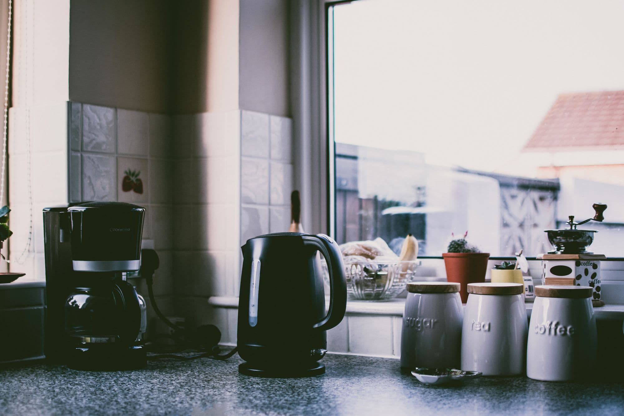 A kitchen counter in soft morning window light, with a kettle and tea and coffee canisters