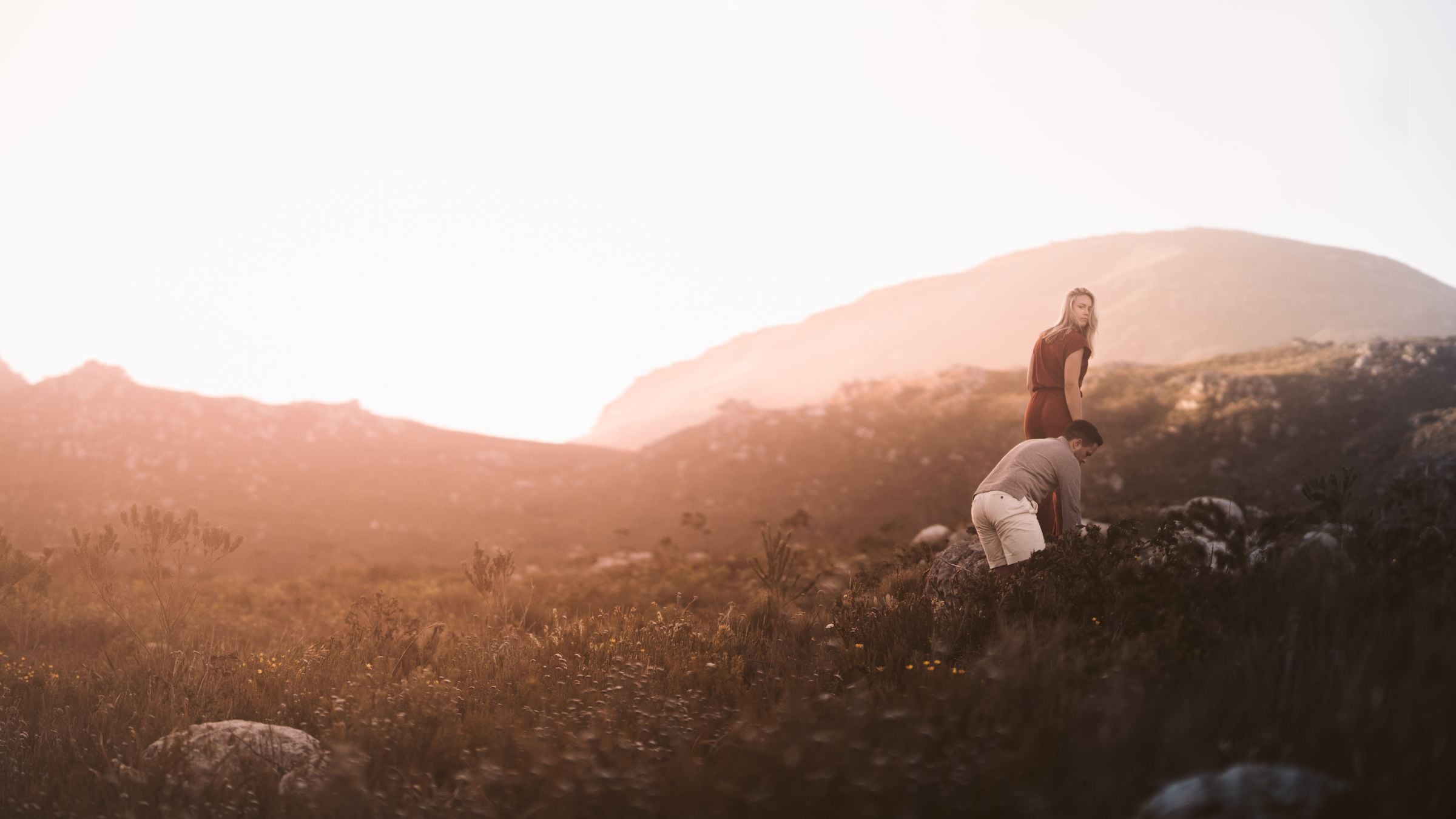 Two people pausing on a hillside of long grass in low golden light